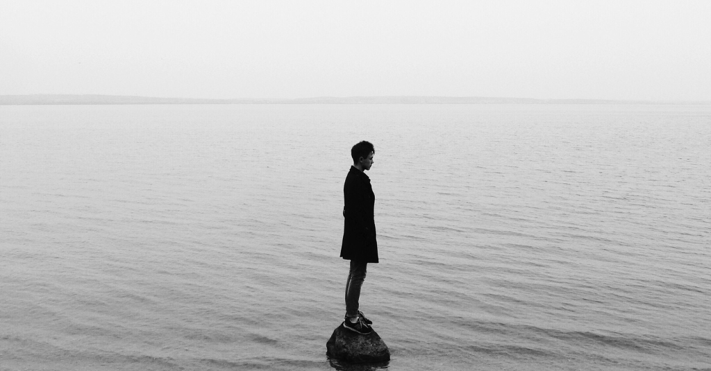 man standing alone in sea on a rock